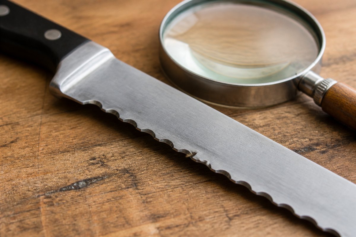 when-a-serrated-knife-needs-repair-not-just-sharpening Close-up of chipped and flattened serrations on a bread knife beside a magnifying glass